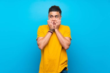 Izole mavi arka plan sinirli üzerinde sarı gömlekli genç adam ve ağız ellerini koyarak korkmuş