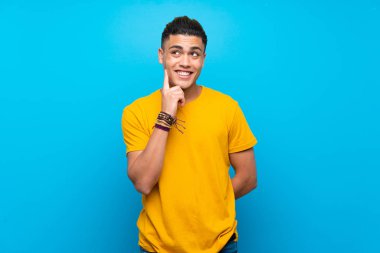 Izole mavi arka plan üzerinde sarı gömlekli genç adam bakarken bir fikir düşünme