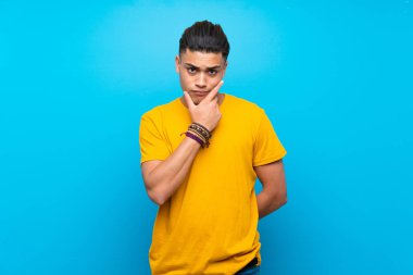 Izole mavi arka plan düşünme üzerinde sarı gömlekli genç adam
