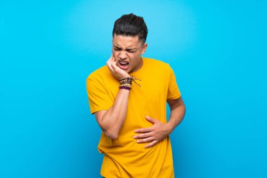Diş ağrısı ile izole mavi arka plan üzerinde sarı gömlekli genç adam