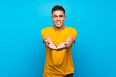 Izole mavi arka plan üzerinde sarı gömlek li genç adam bir reklam eklemek için avuç içinde copyspace hayali tutan