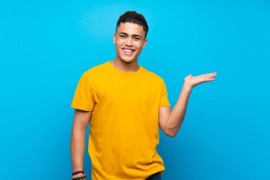 Izole mavi arka plan üzerinde sarı gömlek li genç adam bir reklam eklemek için avuç içinde copyspace hayali tutan