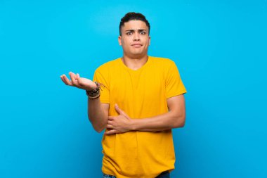 Izole mavi arka plan üzerinde sarı gömlek li genç adam bir şey anlamak için mutsuz