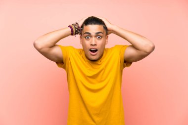 Sürpriz yüz ifadesi ile izole pembe duvar üzerinde sarı gömlekli genç adam
