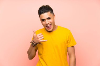 Izole pembe duvar üzerinde sarı gömlekli genç adam telefon jestyapma