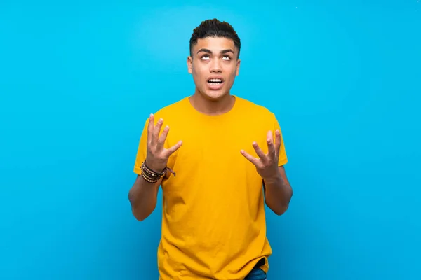 Young man with yellow shirt over isolated blue background frustrated by a bad situation