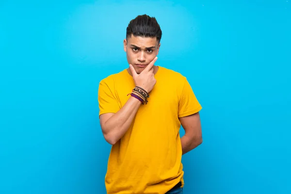 Young man with yellow shirt over isolated blue background thinking