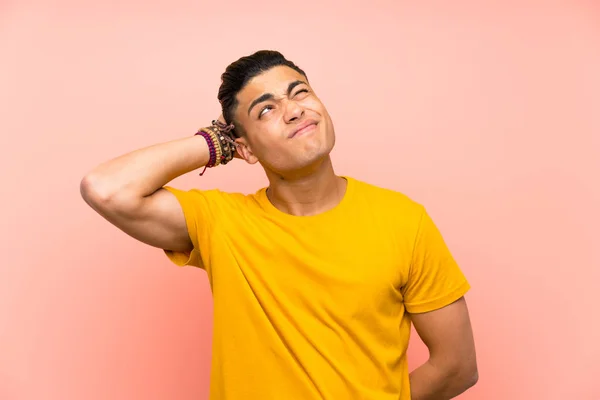 Young man with yellow shirt over isolated pink wall having doubts and with confuse face expression