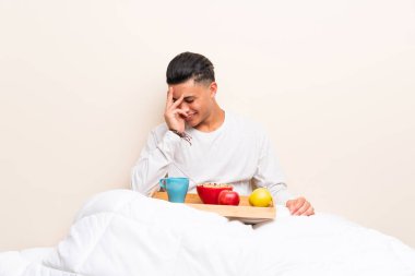 Yatakta gülerek kahvaltı alan genç adam