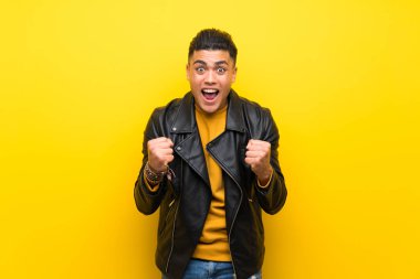 Izole sarı arka plan üzerinde genç adam kazanan pozisyonda bir zafer kutluyor