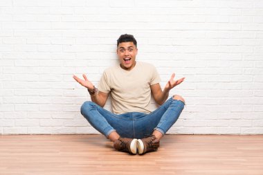 Genç bir adam yerde oturuyor ve yüzünde sürpriz bir ifade var.