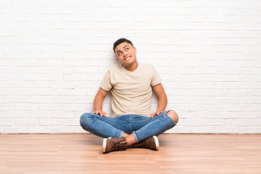 Genç adam yerde gülerek ve yukarı bakarak oturuyor