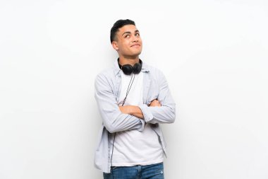 Gülümserken kulaklıklı izole beyaz duvarın üzerinde genç adam yukarı bakıyor