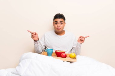 Yatakta kahvaltı eden genç adam, yanların şüphelerine işaret ediyor.