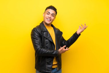 Izole sarı arka plan üzerinde genç adam gelmeye davet için yan ellerini uzatan