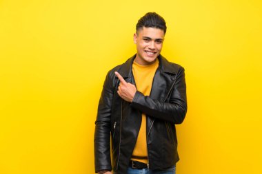 Izole sarı arka plan üzerinde genç adam bir ürün sunmak için yan işaret