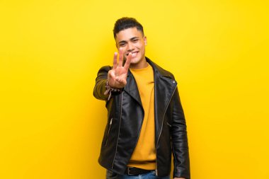 Izole sarı arka plan üzerinde genç adam mutlu ve parmakları ile üç sayma