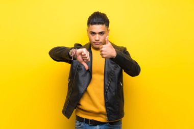 Izole sarı arka plan üzerinde genç adam iyi-kötü işareti yapıyor. Evet ya da değil arasında kararsız