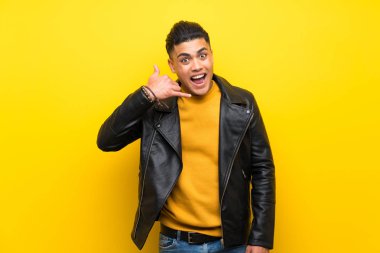 Izole sarı arka plan üzerinde telefon jest yapma genç adam. Beni geri arayın işareti