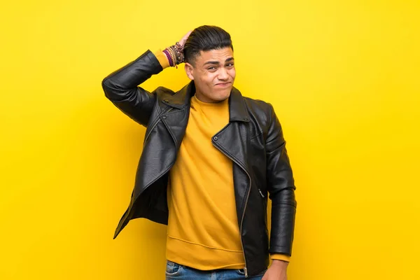Young man over isolated yellow background having doubts while scratching head