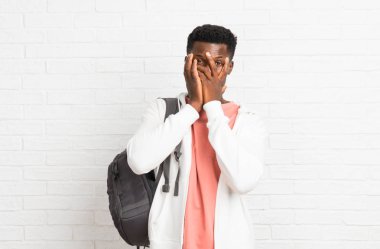 Genç afro Amerikan adam öğrenci elleriyle gözleri kaplayan ve parmaklardan bakarak