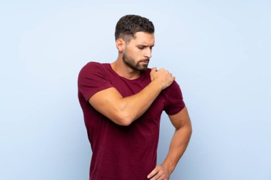 Tecrit edilmiş mavi arka planda yakışıklı bir adam omuz ağrısından muzdarip.
