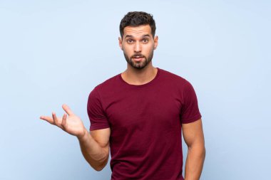 Soyutlanmış mavi arka planda yakışıklı bir adam şüpheli hareketler yapıyor.