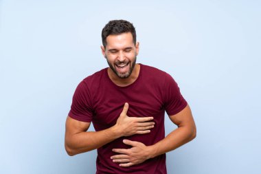 Yakışıklı, soyutlanmış mavi arka planda çok gülümseyen bir adam.