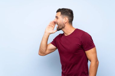 Izole mavi arka plan üzerinde Yakışıklı adam yanal açık ağız ile bağırarak