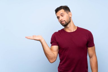 İzole edilmiş mavi arkaplan üzerinde yakışıklı bir adam. Kopyalama alanını şüpheyle tutuyor.