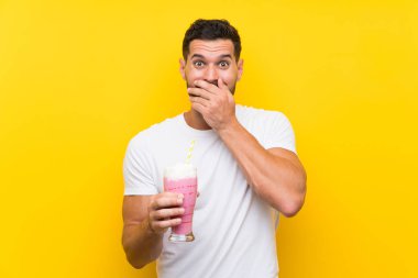 Sürpriz yüz ifadesi ile izole sarı arka plan üzerinde çilek milkshake ile genç adam