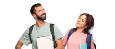 Sırt çantaları ve kitapları ile kalça kolları ile poz ve izole beyaz arka plan üzerinde gülen iki öğrenci