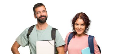 Sırt çantaları ve kitapları ile kalça kolları ile poz ve izole beyaz arka plan üzerinde gülümseyen iki öğrenci