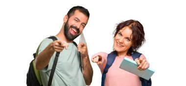 Sırt çantaları ve kitapları olan iki öğrenci izole beyaz arka planda gülümserken sizi işaret ediyor