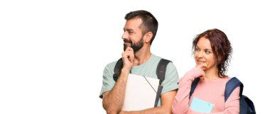 Sırt çantaları ve kitaplar izole beyaz arka plan üzerinde çene üzerinde el ile yan bakarak iki öğrenci