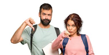 Sırt çantaları ve izole beyaz arka plan üzerinde olumsuz ifade ile başparmak aşağı işareti gösteren kitaplar ile iki öğrenci