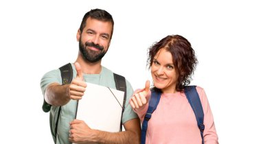 Sırt çantaları ve kitapları olan iki öğrenci başparmak kadar jest veren ve izole beyaz arka plan üzerinde gülümseyen
