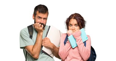 Sırt çantaları ve kitapları olan iki öğrenci biraz gergin ve izole beyaz arka plan üzerinde ağız ellerini koyarak korkuyor