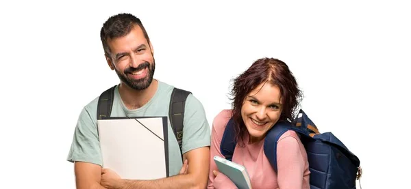Two students with backpacks and books keeping the arms crossed while smiling on isolated white background