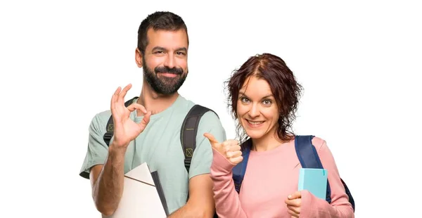 两名学生背着背包和书籍 在孤立的白色背景上用另一只手竖起大拇指 — 图库照片
