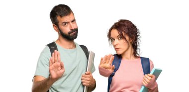 Sırt çantaları ve kitapları olan iki öğrenci eliyle jest yaparak izole beyaz arka planda yanlış düşünen bir durumu inkar ediyor.