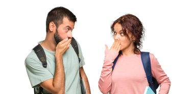 Sırt çantaları ve kitapları ile iki öğrenci izole beyaz arka plan üzerinde uygunsuz bir şey söylemek için elleri ile ağız kapsayan