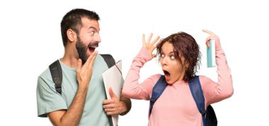 Izole beyaz arka plan üzerinde sürpriz ve şok yüz ifadesi ile sırt çantaları ve kitapları ile iki öğrenci