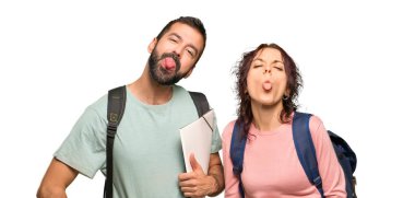 Sırt çantaları ve izole beyaz arka plan üzerinde komik bir görünüme sahip kamera dil gösteren kitaplar ile iki öğrenci