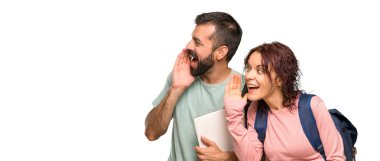 Sırt çantaları ve kitapları lateral bağırarak ve izole beyaz arka plan üzerinde bir şey ilan ile iki öğrenci