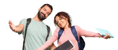 Sırt çantaları ve kitapları sunan ve gelmeye davet eden iki öğrenci. İzole beyaz arka planda geldiğiniz için mutlusunuz.