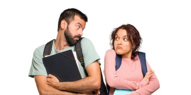 Sırt çantaları ve kitapları olan iki öğrenci, izole beyaz arka plan üzerinde omuzlarını kaldırırken önemsiz bir jest yapıyor