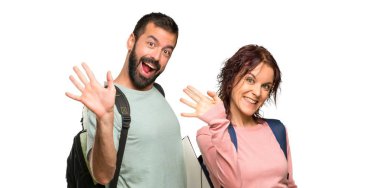 Sırt çantaları ve kitaplar izole beyaz arka plan üzerinde mutlu ifade ile el ile selamlama ile iki öğrenci