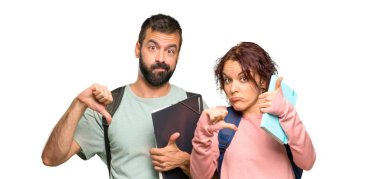 Sırt çantaları ve kitapları olan iki öğrenci iyi-kötü işareti yapıyor. İzole beyaz arka planda evet veya değil arasında kararsız