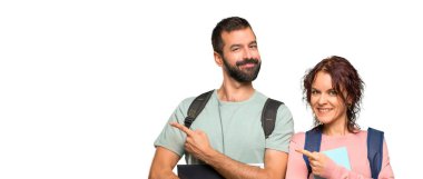 Yalıtılmış beyaz arka plan üzerinde bir ürün sunmak için bir parmak ile yan işaret sırt çantaları ve kitapları ile iki öğrenci